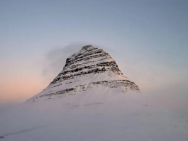 A snow-covered, pyramid-shaped mountain rises against a pale winter sky.