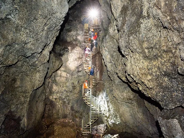 People descending a spiral staircase inside Vatnshellir Cave with lighting.