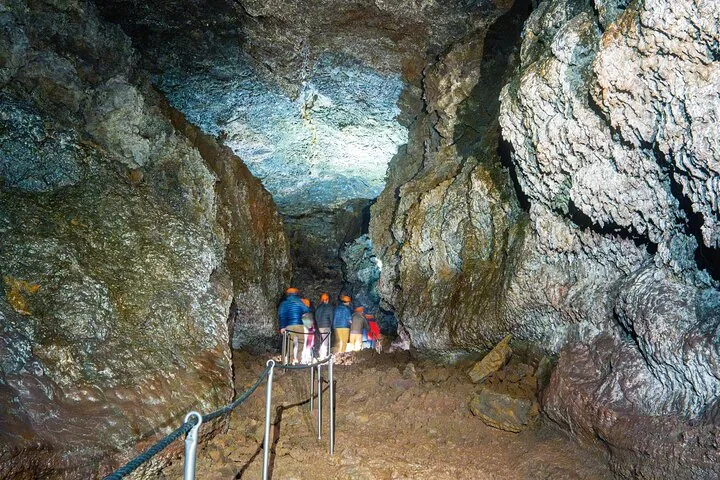 Group of tourists walking on a path inside the illuminated Vatnshellir Cave.
