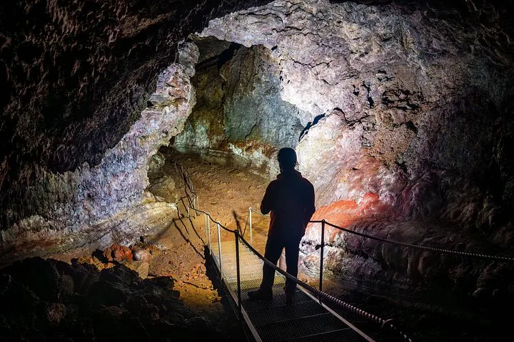 Person standing on a metal walkway inside the dark Vatnshellir Cave.