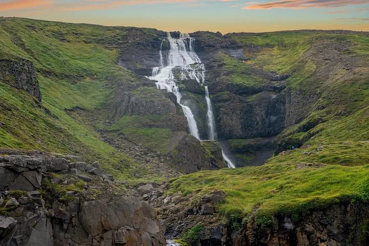 Waterfall cascading down a rocky, green cliffside in Iceland