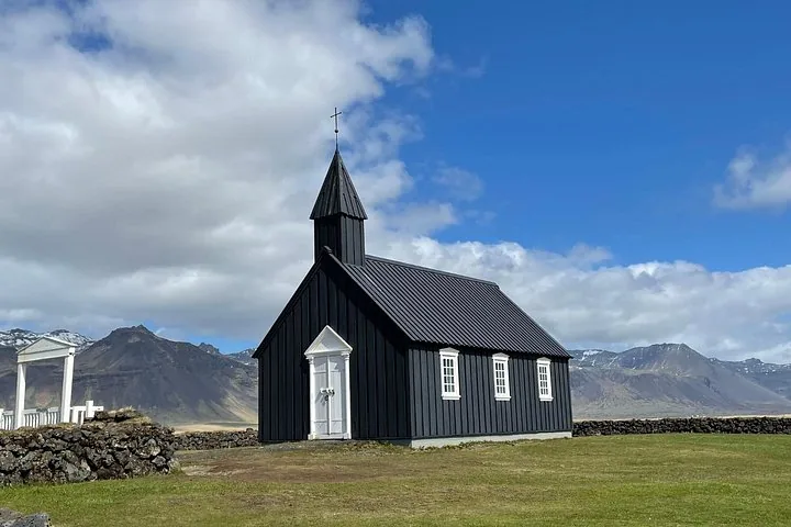 Black wooden church surrounded by green fields and distant mountains