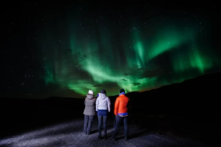 Three people watching the northern lights in a dark landscape